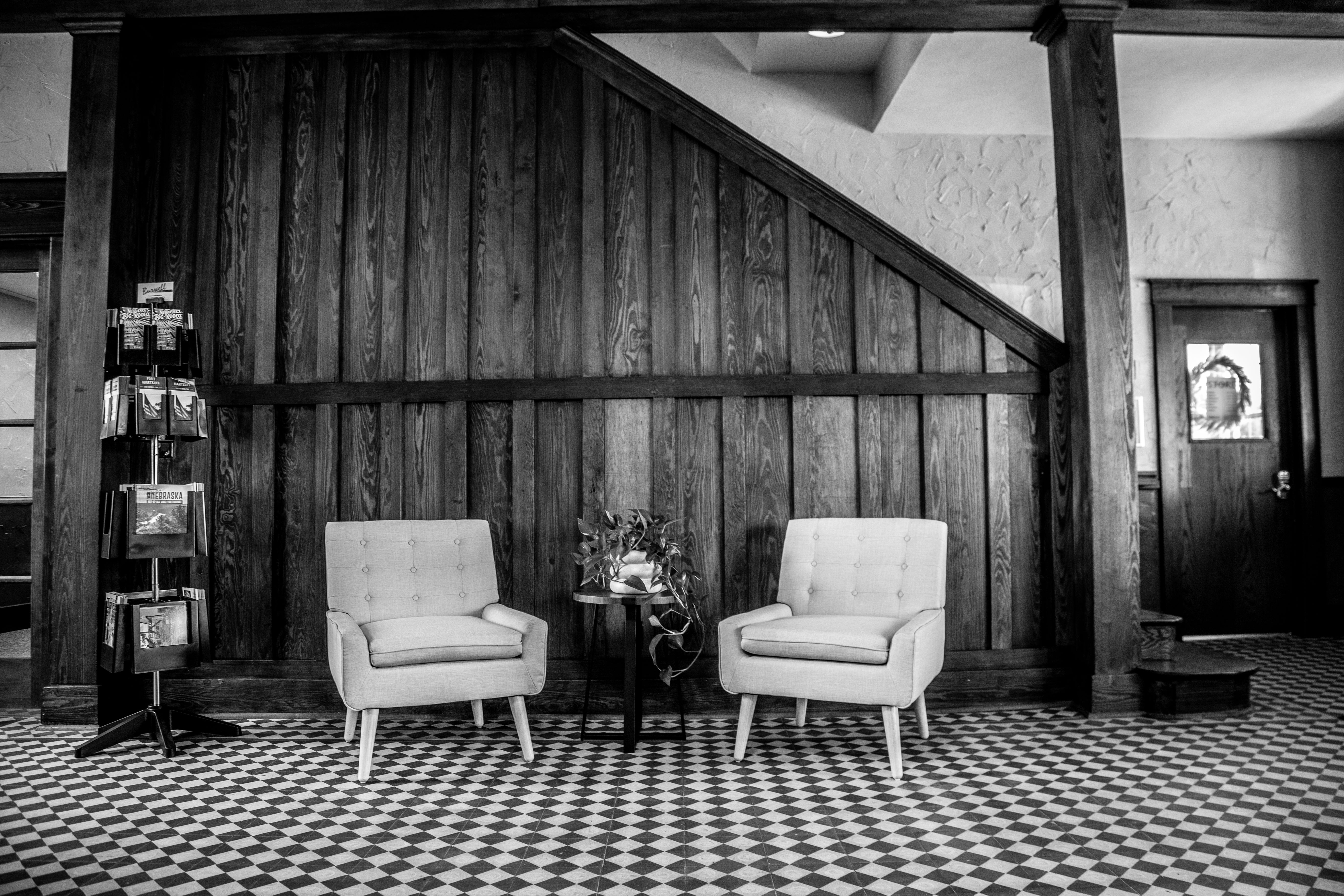 A lobby seating area with two armchairs, a small table, and a magazine rack in front of a wood-paneled wall.