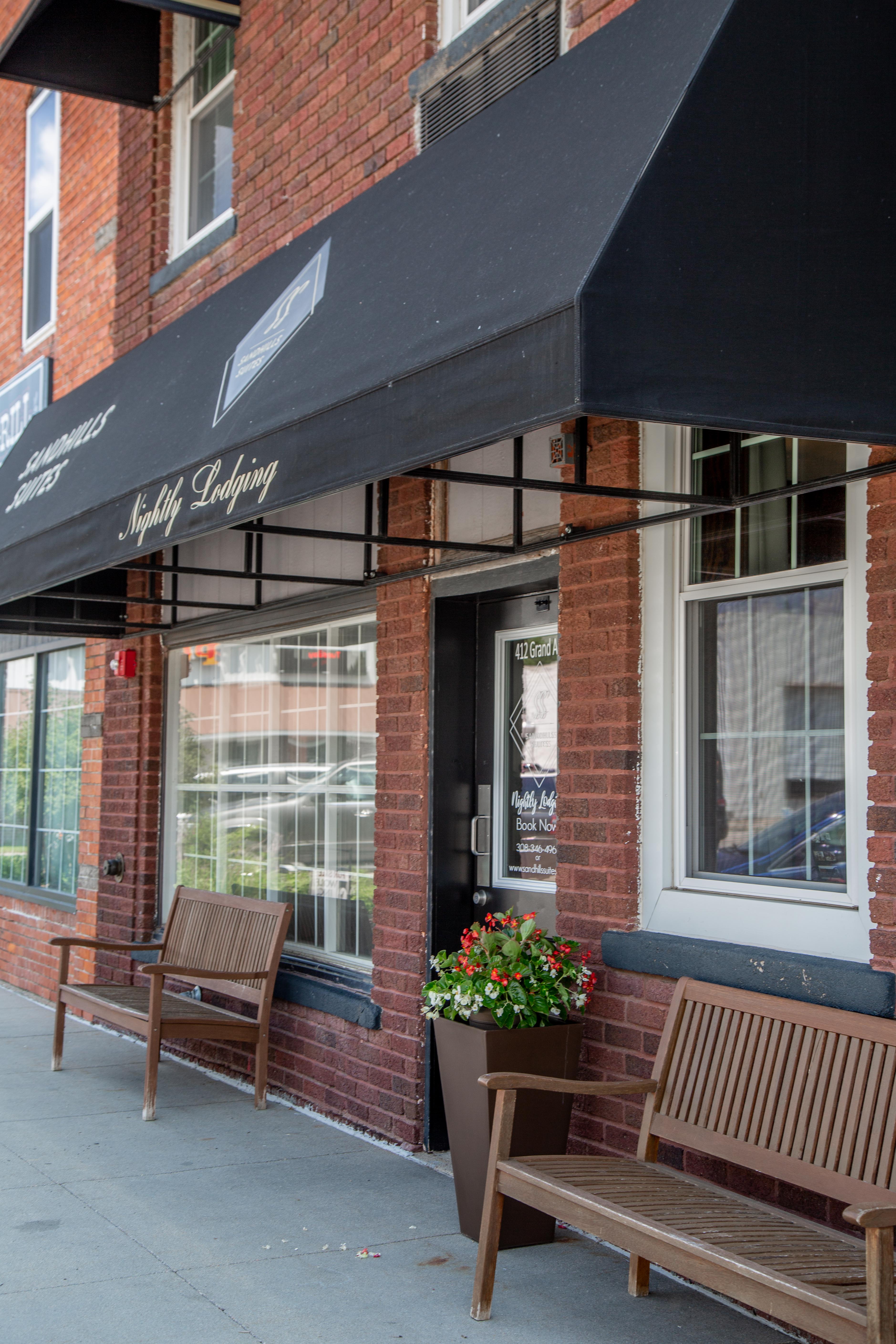 A red brick building with a black awning and two wooden benches outside the entrance.