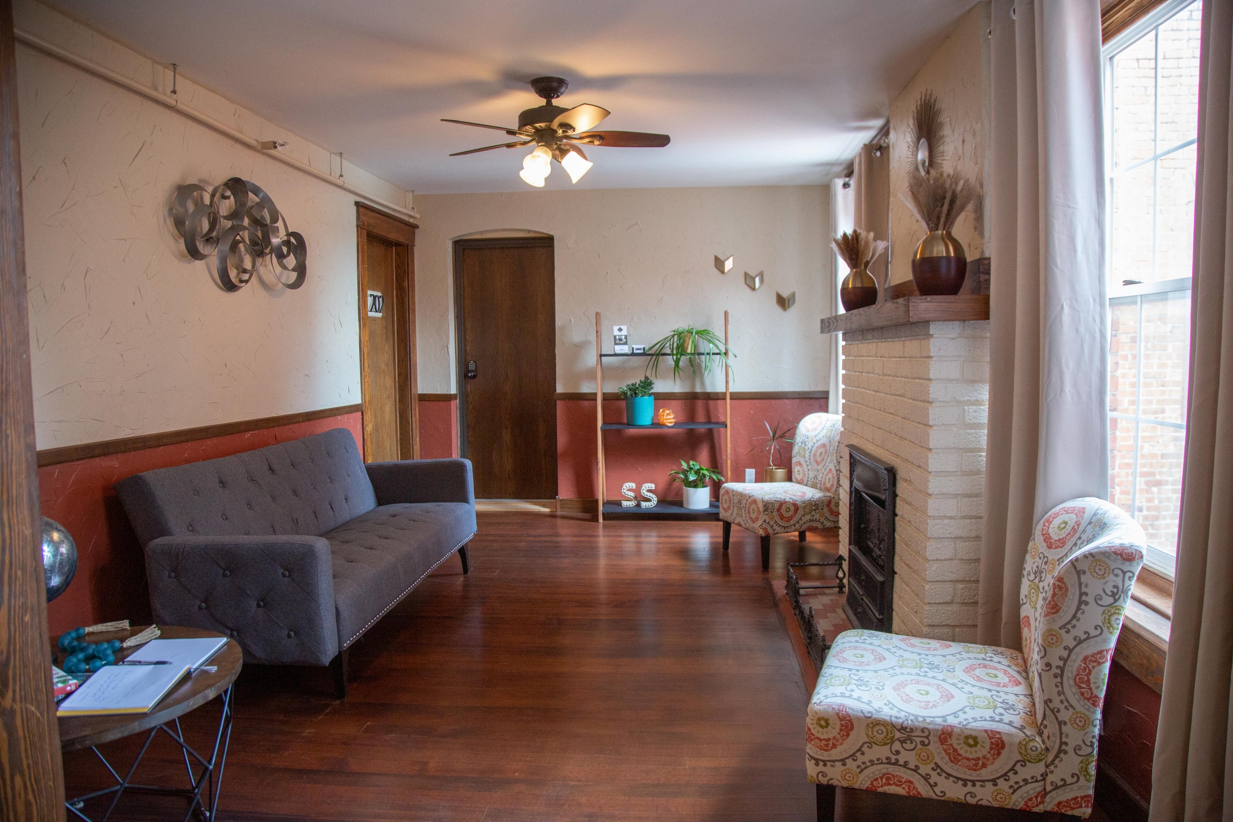 A cozy lobby with a gray sofa, patterned armchair, and a white brick fireplace.
